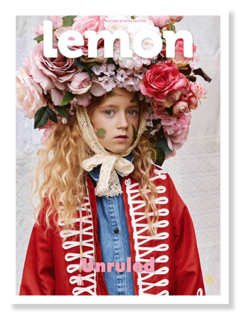 Child wearing a large floral headpiece, lace bonnet ties, denim shirt, and red military-style jacket with white braid trim.