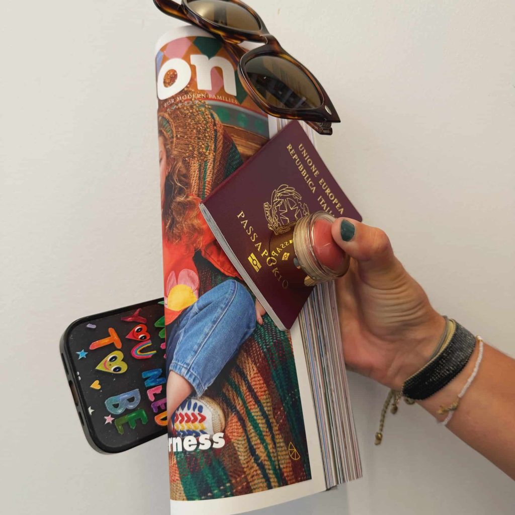 Hand holding sunglasses, a passport and a phone on top of a rolled copy of Lemon magazine